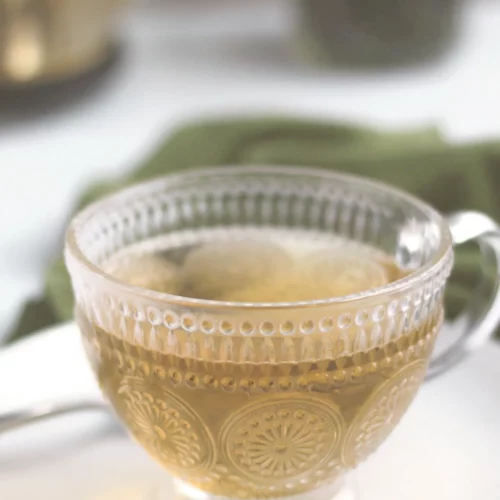 Peppermint tea in a glass and a teapot in the background.