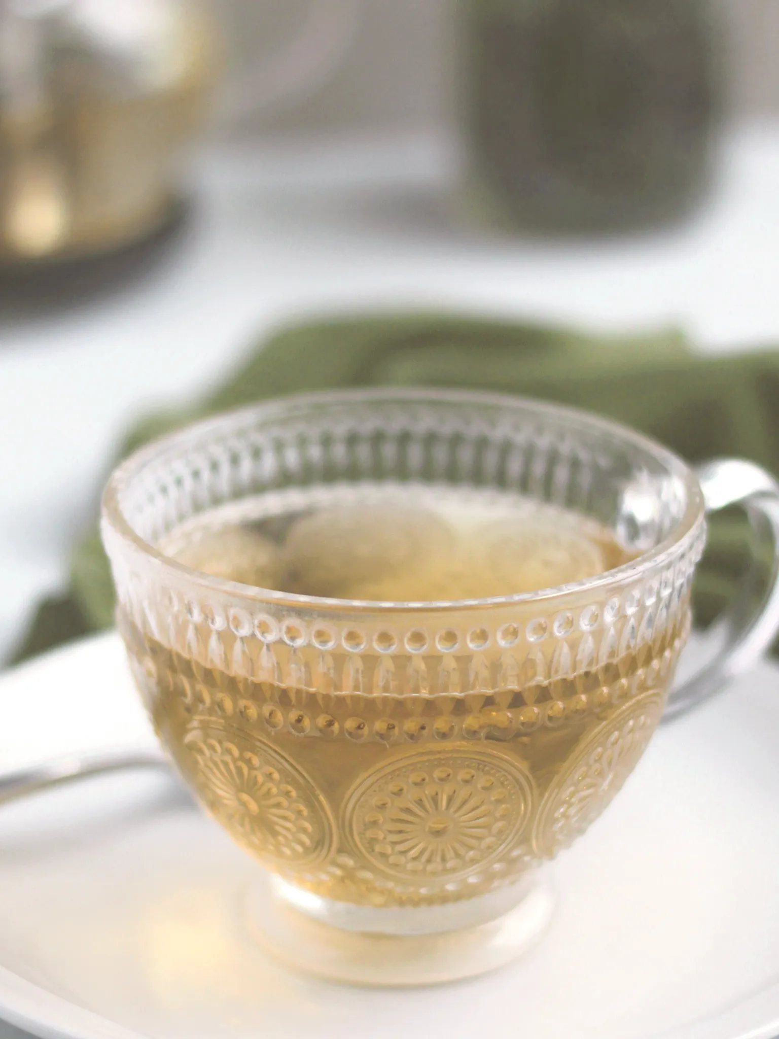 Peppermint tea in a glass and a teapot in the background.