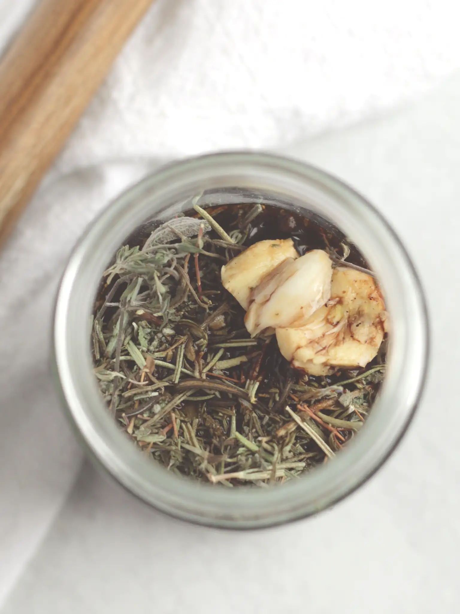 Close-up of dried herbs and a smashed garlic clove in a glass jar filled with balsamic vinegar.