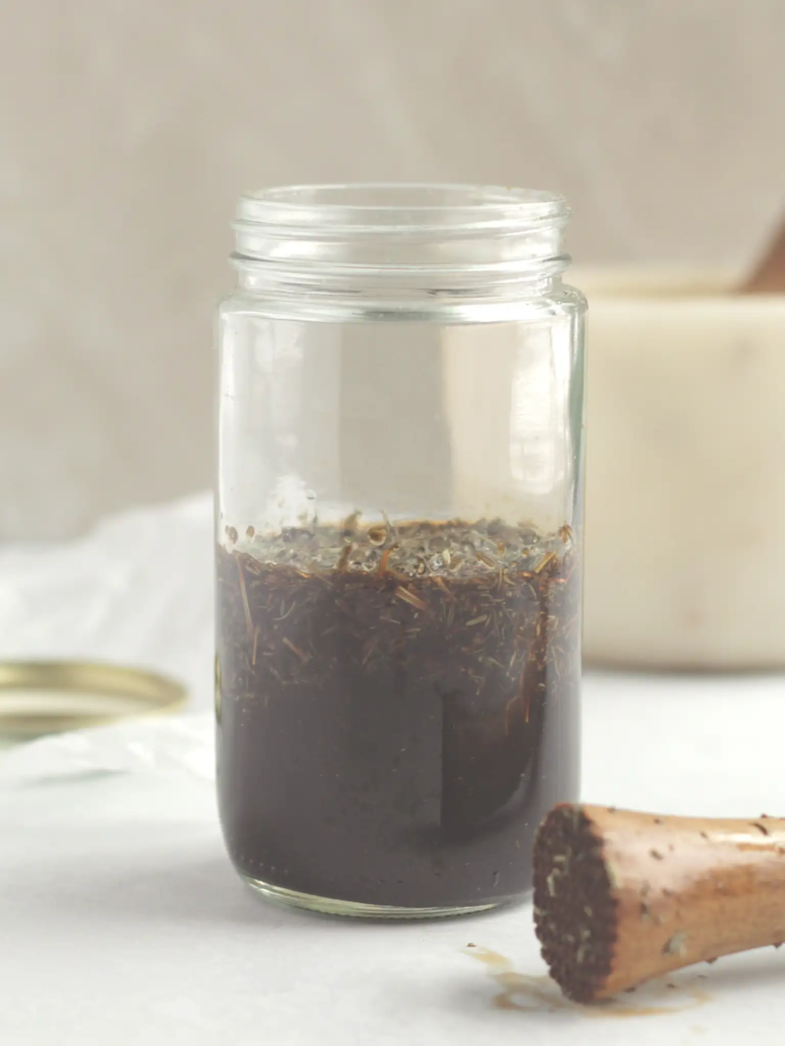 Dried herbs and a smashed garlic clove in a glass jar filled with balsamic vinegar.