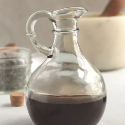 Garden herb balsamic vinegar in a glass vinegar jar on a counter.