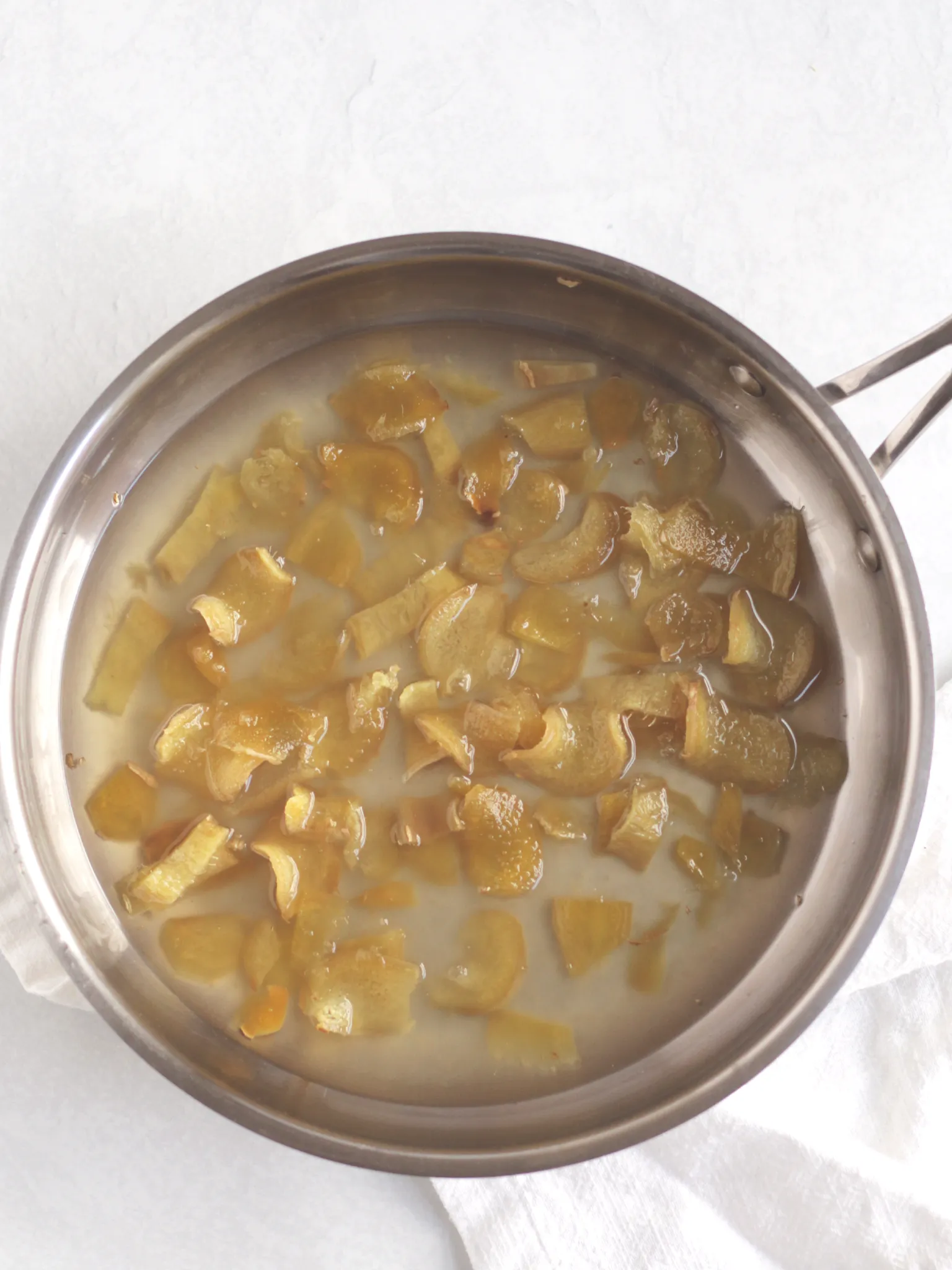 Cooked ginger slices in a water and sugar mixture in a metal pan