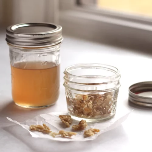 Ginger syrup in a mason jar next to a jar of crystallized ginger.