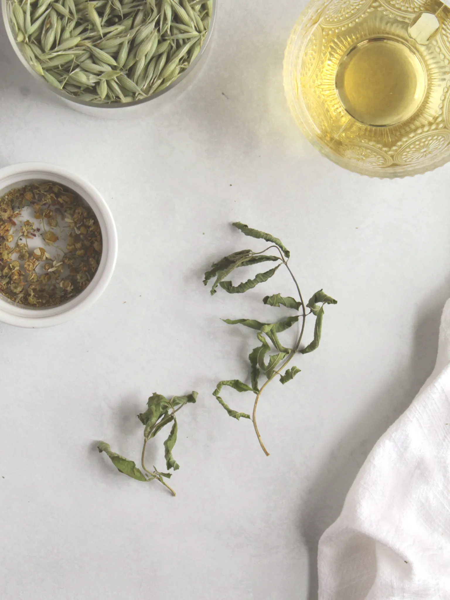 Lemon verbena tea with dried oat tops, dried chamomile, and dried lemon verbena on a table.