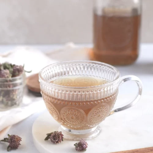 Red clover tea in a glass cup on a table with dried red clover flowers