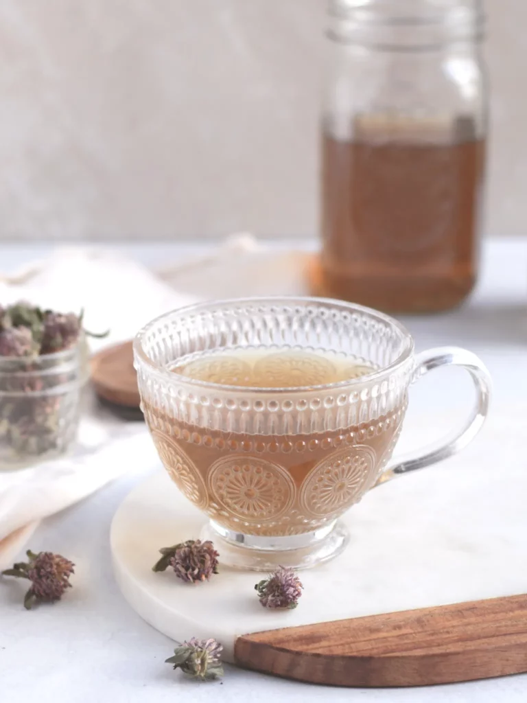 Red clover tea in a glass cup on a table with dried red clover flowers