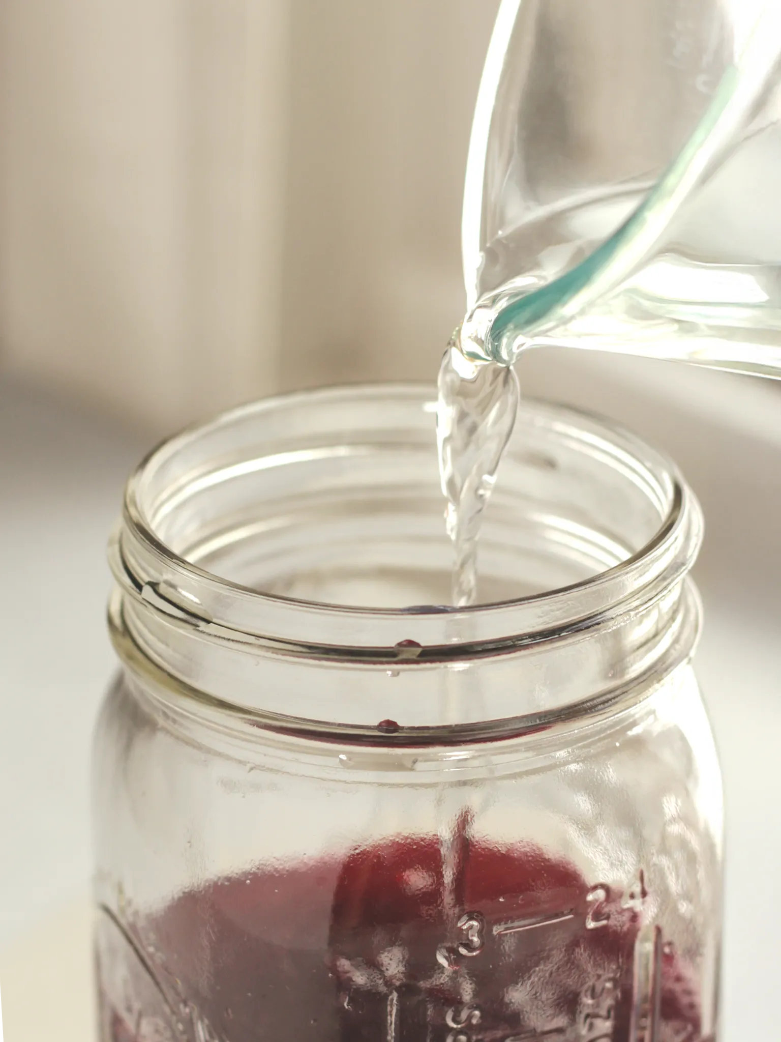 White wine vinegar pouring into a Mason jar containing blueberry lavender syrup.