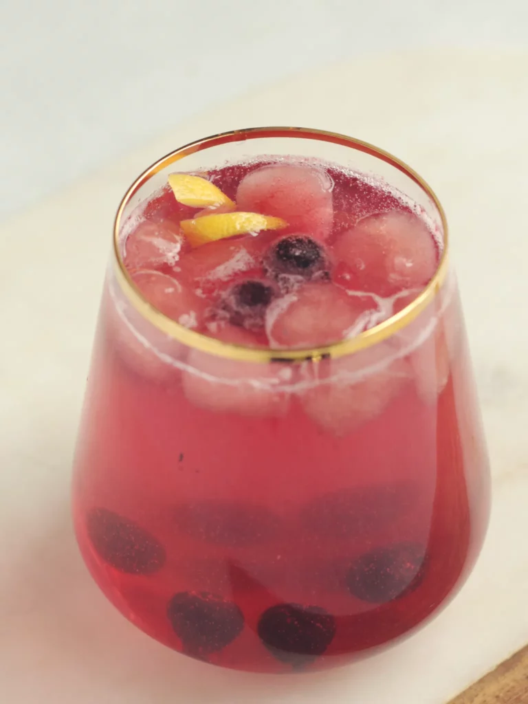 A cocktail glass with gold rim containing blueberry lavender mocktail. There are blueberries and a lemon peel as garnish.