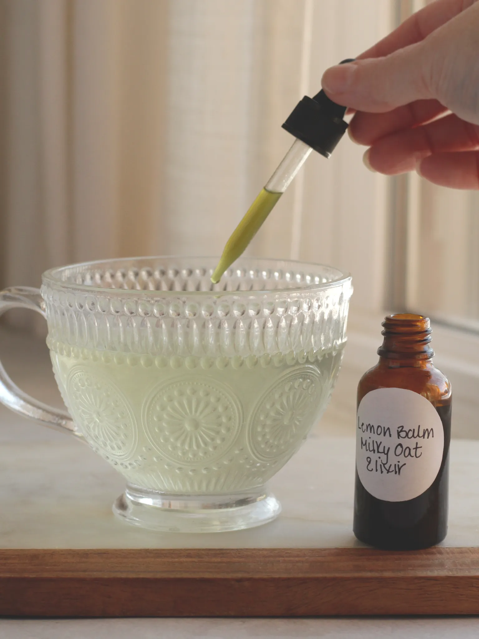 A hand squeezing lemon balm and milky oat elixir into a glass of water.