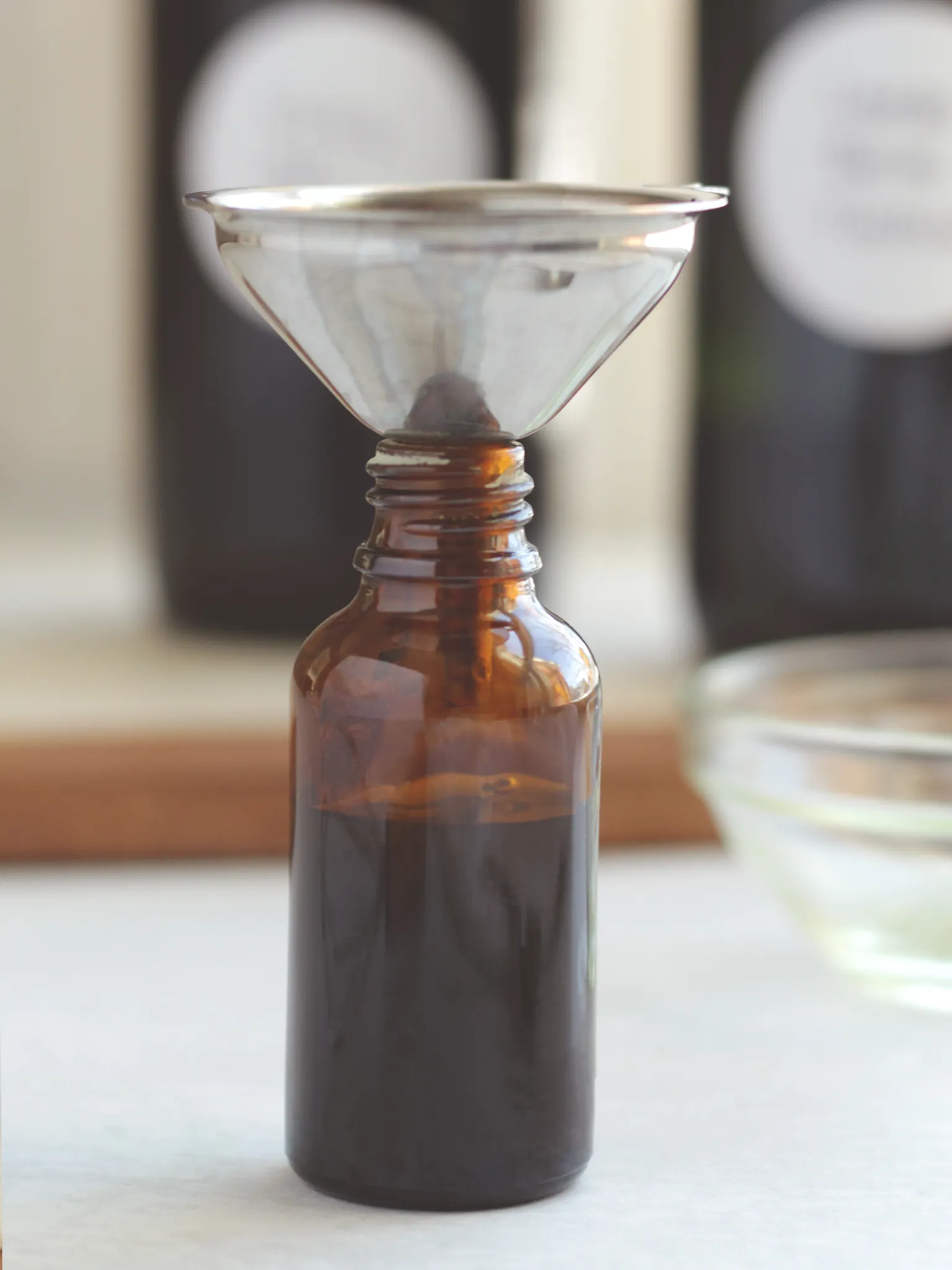 A one ounce amber glass bottle with a metal funnel resting in the top of the bottle.