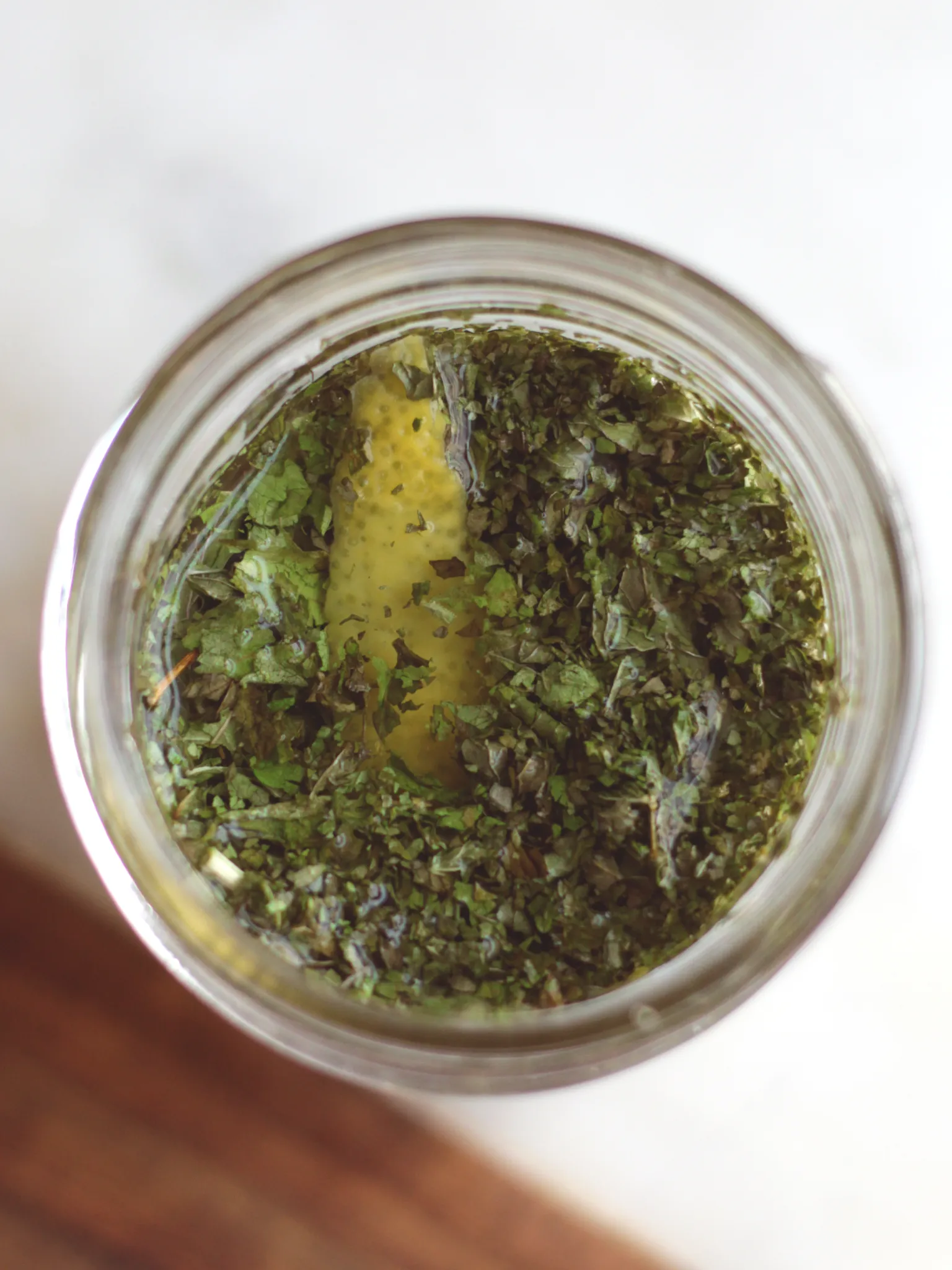 Overhead view of a Mason jar filled with Champagne vinegar, lemon verbena, sweet mint, and a lemon peel.