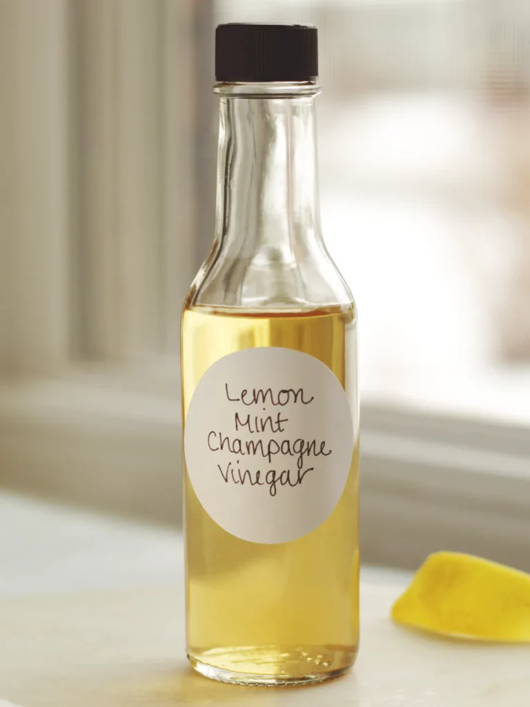 A clear bottle of lemon mint champagne vinegar on a white table next to a lemon peel.