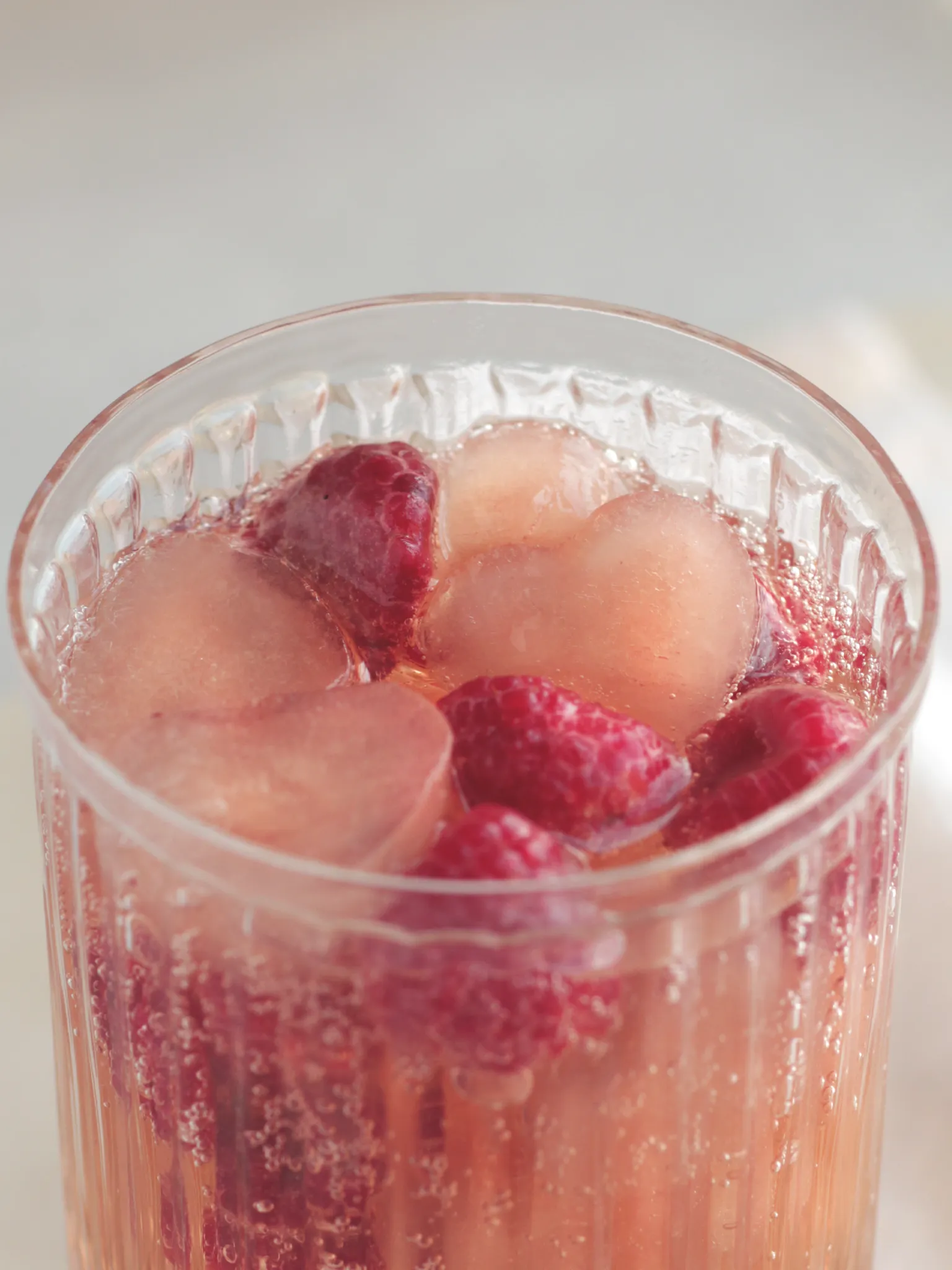 A glass filled with heart shaped ice cubes, frozen raspberries and a fizzy drink.