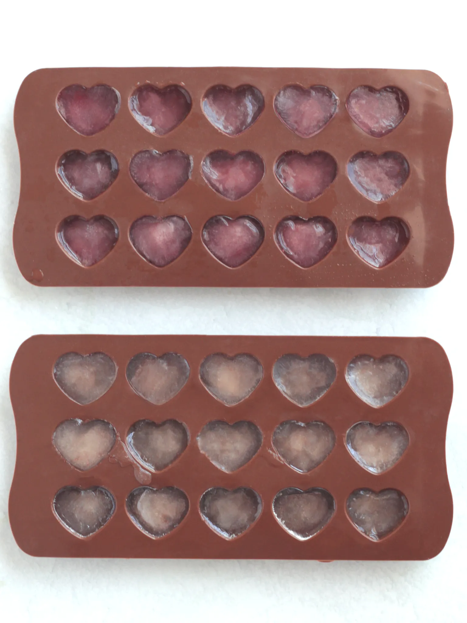 Two heart shaped silicone molds filled with pink colored rose tea. The tea is frozen into ice cubes.