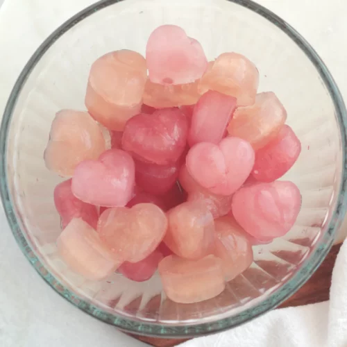 A glass bowl filled with heart shaped ice cubes of varying shades of pink