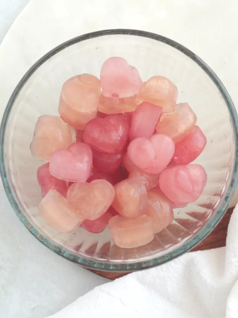 A glass bowl filled with heart shaped ice cubes of varying shades of pink