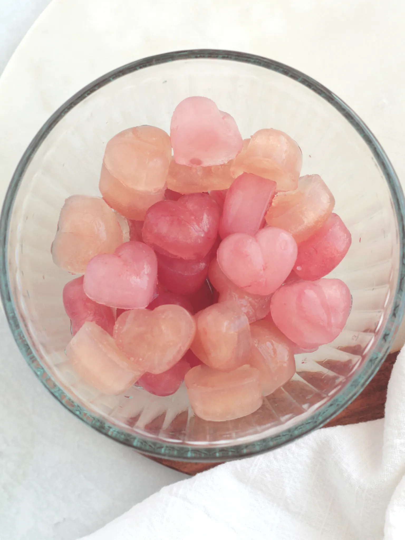 A glass bowl filled with heart shaped ice cubes of varying shades of pink