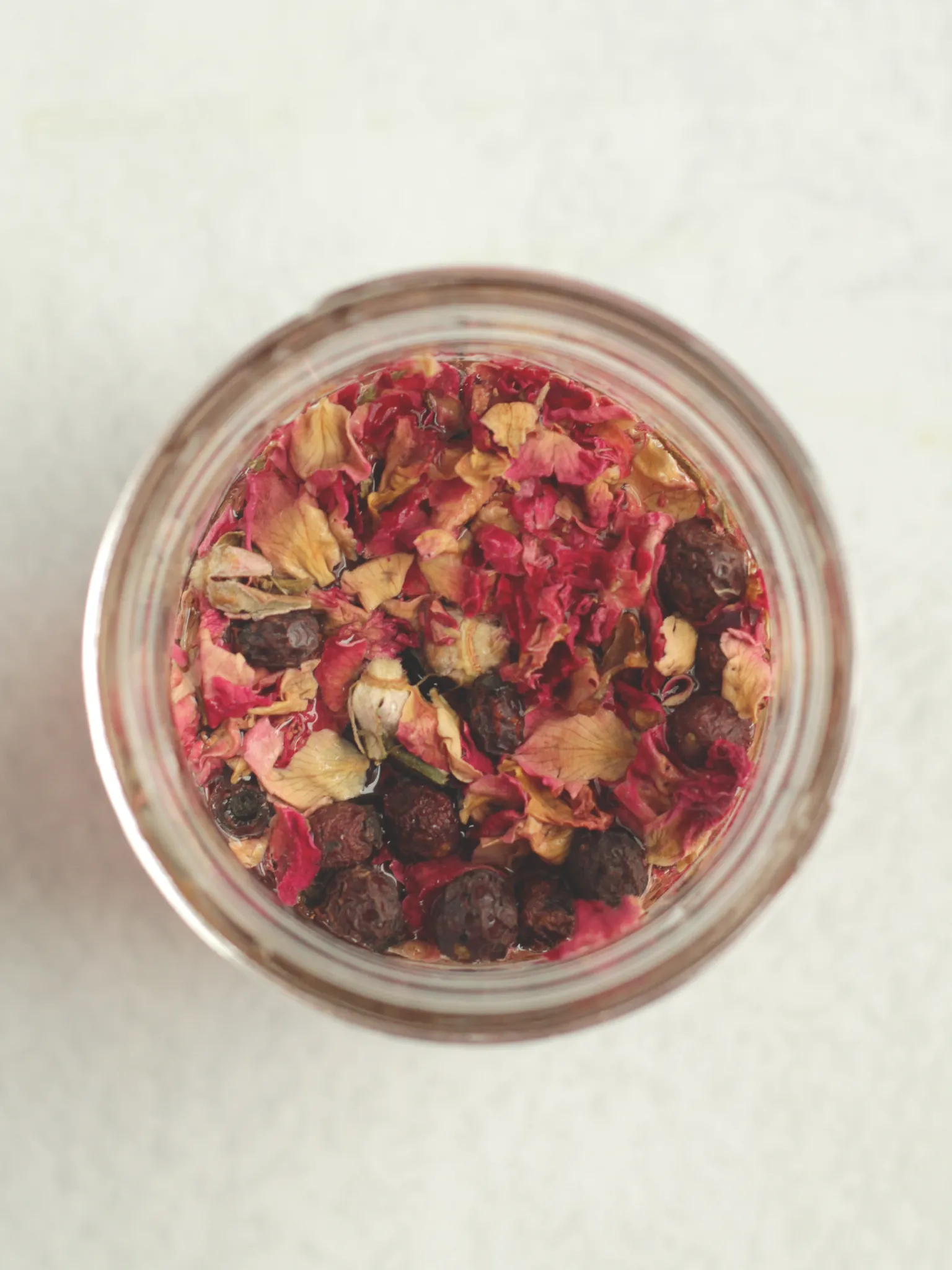 Overhead shot of a Mason jar filled with Champagne vinegar, dried roses, and dried hawthorn berries.