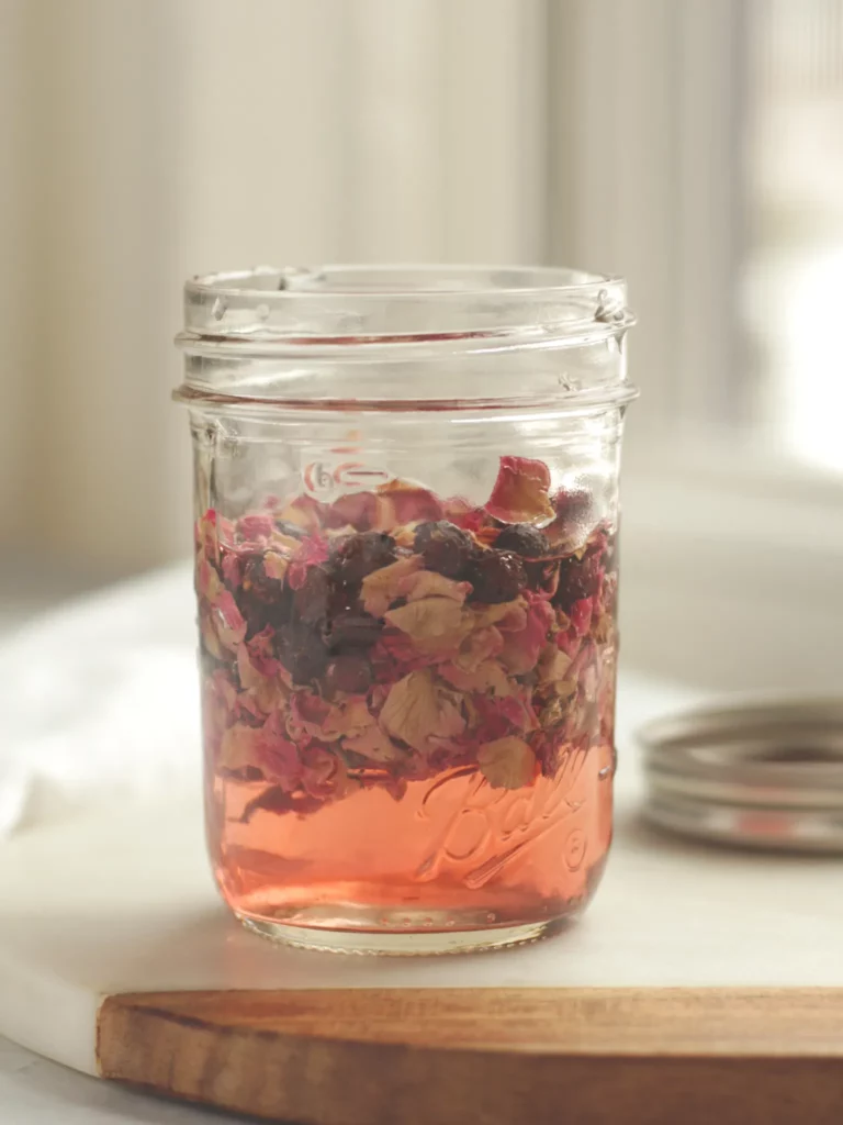 A Mason jar filled with Champagne vinegar, dried roses, and dried hawthorn berries.