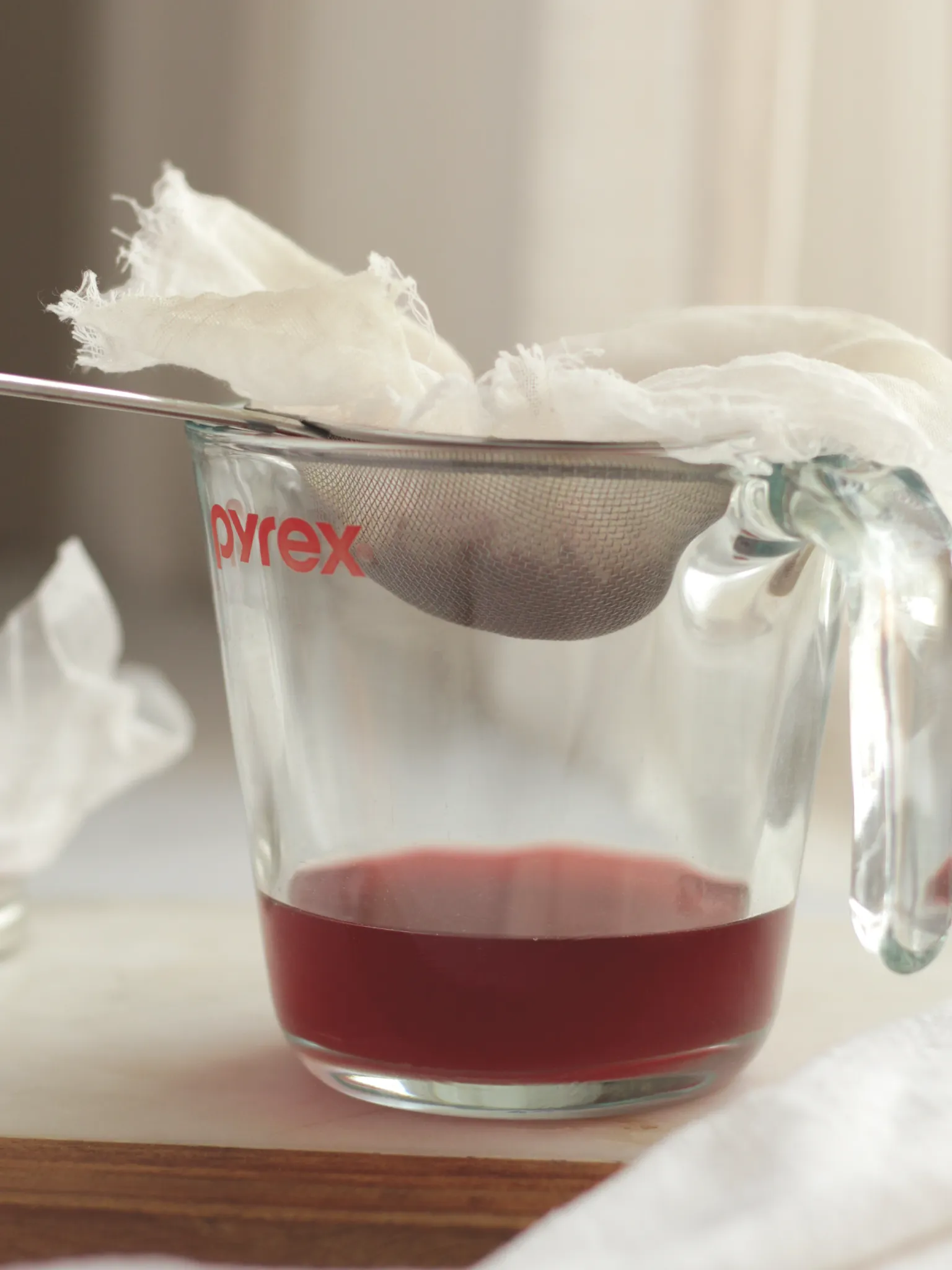 A glass measuring cup with a cheesecloth lined fine mesh strainer. The measuring cup contains the finished Champagne vinegar infusion.