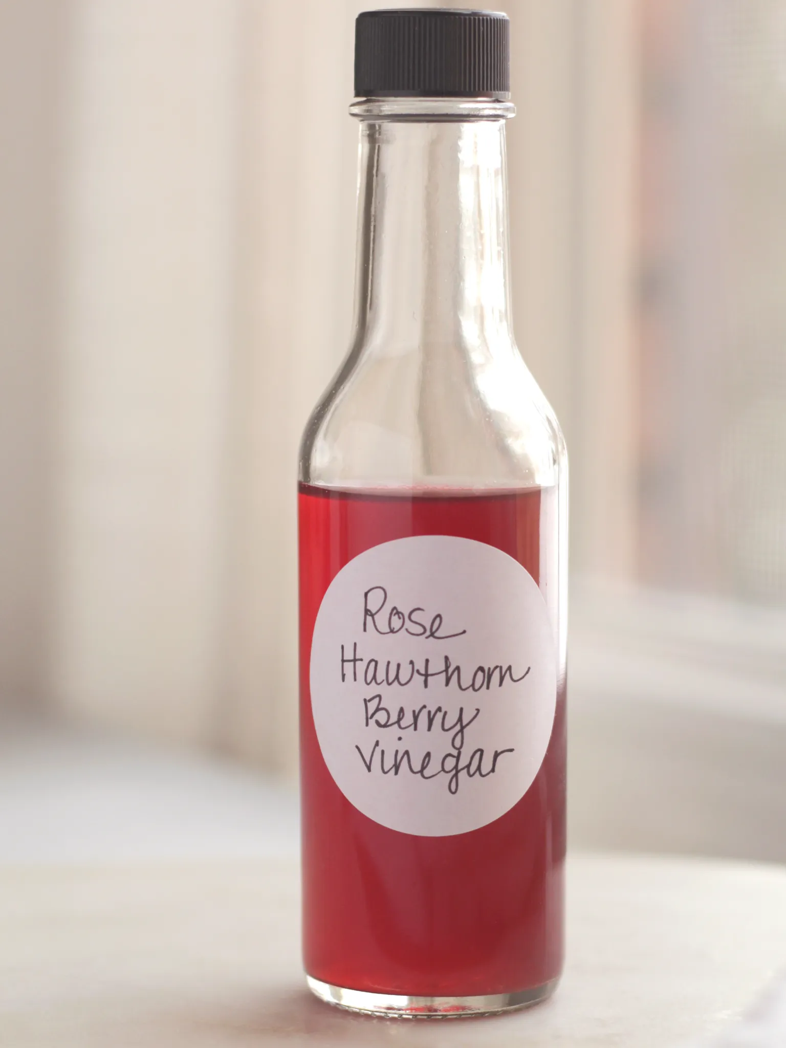 A glass bottle filled with the finished rose and hawthorn berry infused Champagne vinegar. The color is a very pretty pinky-red.